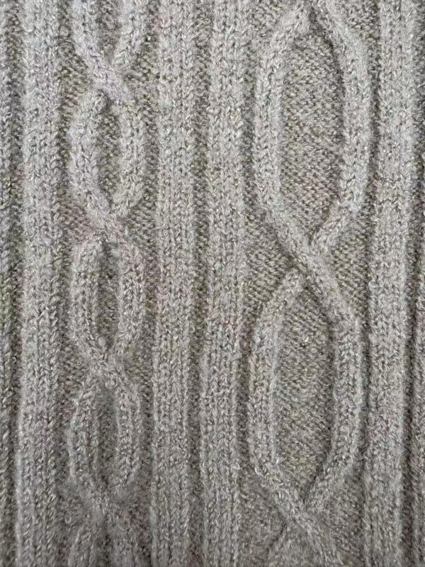 Close-up of a cable knit sweater fabric in neutral tones, showcasing intricate knitting patterns and textured design.