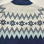 Close-up of a Nordic patterned sweater with snowflake and zigzag designs in navy blue and light blue on a cream background.
