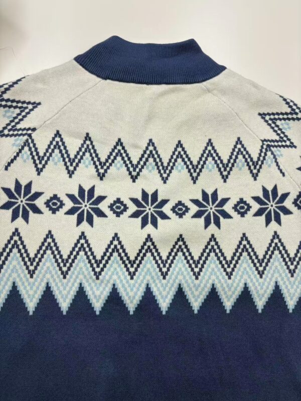 Close-up of a Nordic patterned sweater with snowflake and zigzag designs in navy blue and light blue on a cream background.
