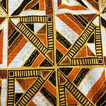 Close-up of vibrant African-inspired fabric with geometric patterns in black, orange, yellow, and white colors, featuring rulers as part of the design.