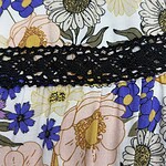 Close-up of a floral dress featuring white, yellow, pink, and purple flowers with a black lace detail across the fabric.
