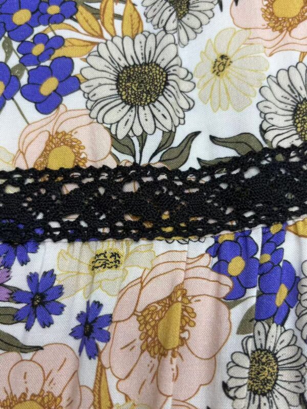 Close-up of a floral dress featuring white, yellow, pink, and purple flowers with a black lace detail across the fabric.