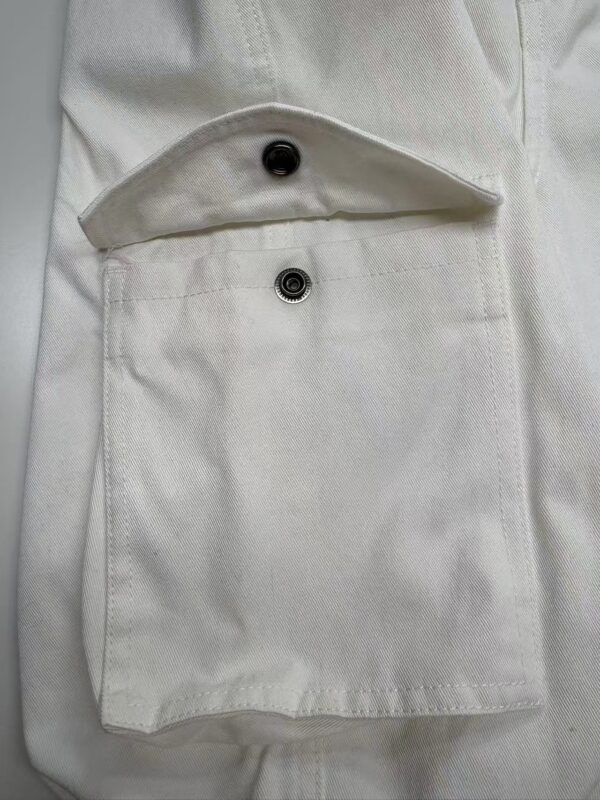 Close-up of a white fabric pocket with a button closure, showcasing fine stitching and clean design, ideal for fashion and clothing product images.