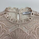Close-up of a delicate, beige lace dress with intricate embroidery and a high neckline, featuring a SUZY brand label.