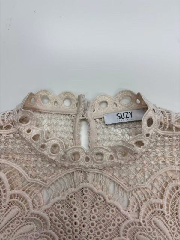 Close-up of a delicate, beige lace dress with intricate embroidery and a high neckline, featuring a SUZY brand label.