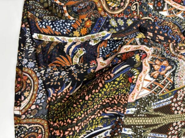 Close-up of vibrant paisley and floral fabric with intricate designs in orange, blue, green, and pink colors, showcasing detailed textile craftsmanship.