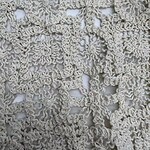 Close-up of detailed cream-colored crochet lace fabric with floral and geometric patterns, ideal for fashion and home decor.