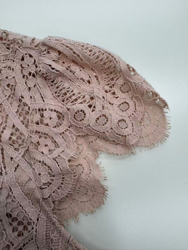 Close-up of delicate pink lace fabric with intricate patterns, ideal for fashion and apparel design, showcasing craftsmanship and fine textile details.