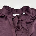 Close-up of a stylish burgundy blouse with a bow tie collar, perfect for fashionable women's wardrobe.