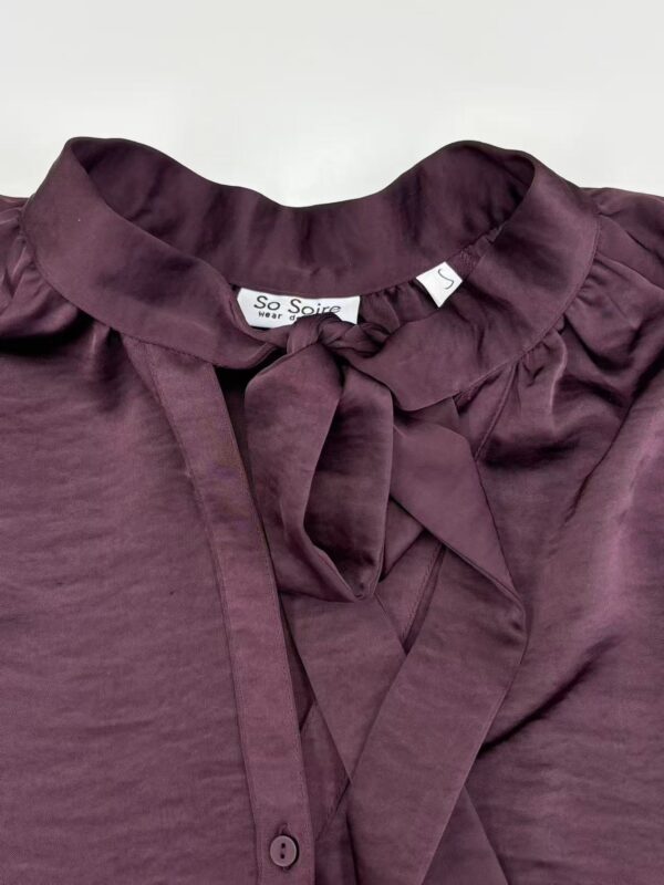 Close-up of a stylish burgundy blouse with a bow tie collar, perfect for fashionable women's wardrobe.