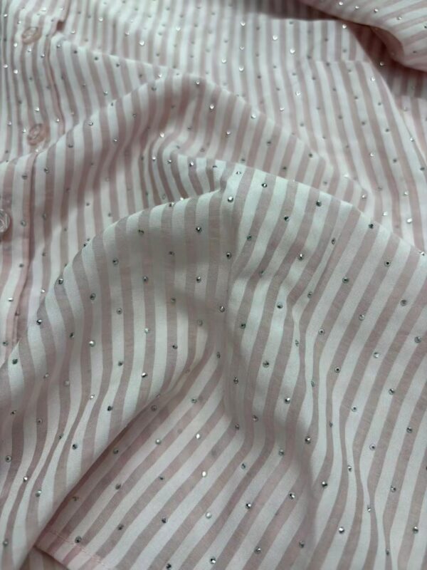 Close-up of a soft pink fabric with white stripes and scattered rhinestones, showcasing a luxurious and delicate texture suitable for fashion design.