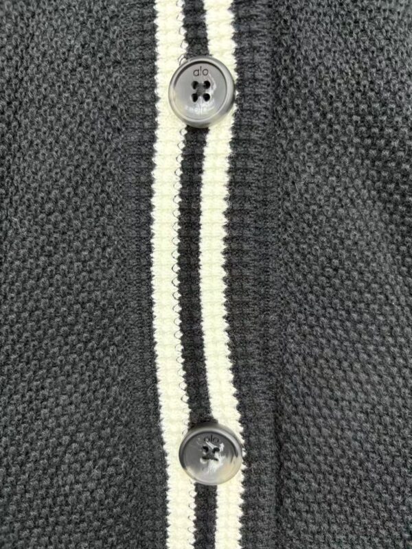Detailed view of a dark gray knit cardigan featuring white and black striped trim and gray buttons, showcasing high-quality fabric and craftsmanship.