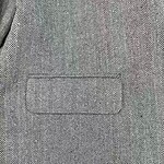 Close-up of men's herringbone suit jacket with front pocket, showcasing classic pattern and tailored fit for formal or business wear.