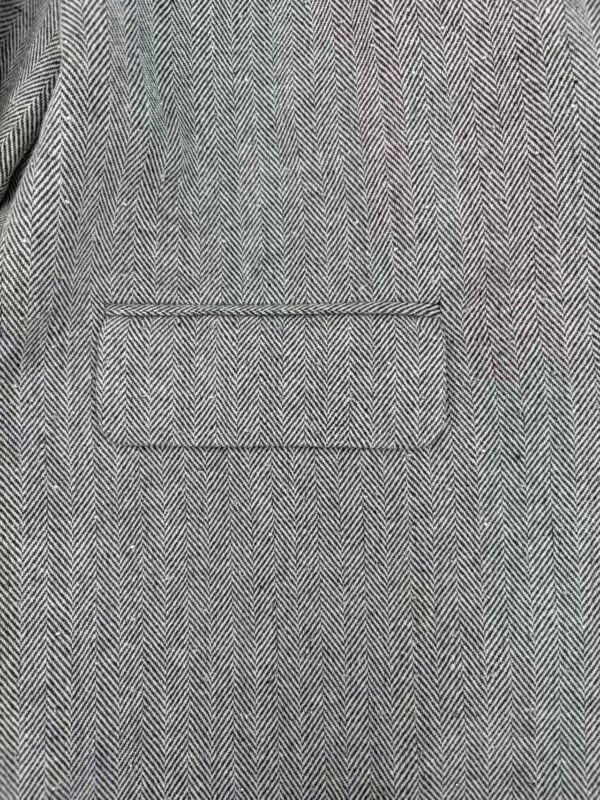 Close-up of men's herringbone suit jacket with front pocket, showcasing classic pattern and tailored fit for formal or business wear.