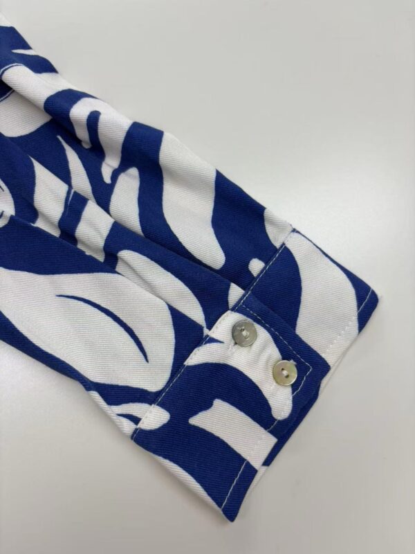 Close-up of a blue and white patterned shirt sleeve with buttons, showcasing fashionable casual wear.
