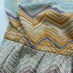 Close-up of vibrant woven textile fabric with zigzag patterns in yellow, purple, green, and beige, suitable for fashion and home decor.
