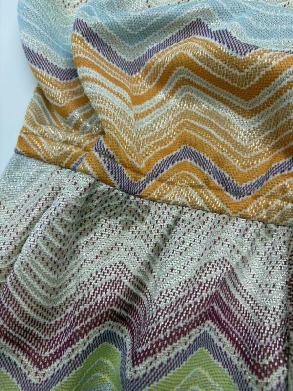 Close-up of vibrant woven textile fabric with zigzag patterns in yellow, purple, green, and beige, suitable for fashion and home decor.