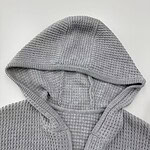 Close-up of a gray waffle knit hoodie with a front zipper and hood, perfect for casual wear and cold weather.