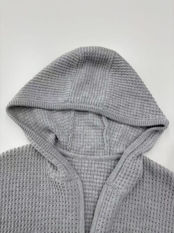 Close-up of a gray waffle knit hoodie with a front zipper and hood, perfect for casual wear and cold weather.