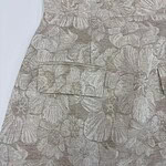 Close-up of a dress with a beige floral pattern featuring large, detailed leaves and subtle pink accents, showcasing sophisticated fabric design.