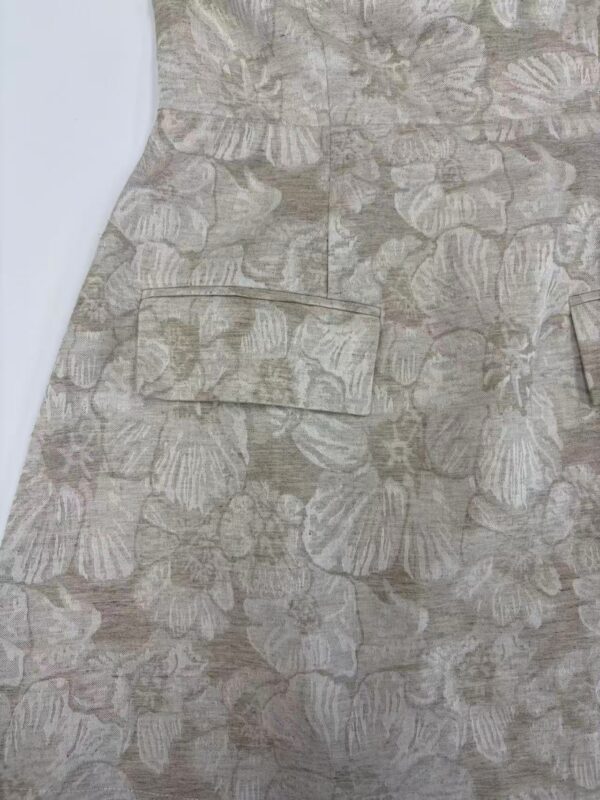 Close-up of a dress with a beige floral pattern featuring large, detailed leaves and subtle pink accents, showcasing sophisticated fabric design.