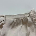 Close-up of a beige satin blouse with gathered shoulder detail, showcasing smooth fabric and subtle sheen, perfect for stylish fashion looks.