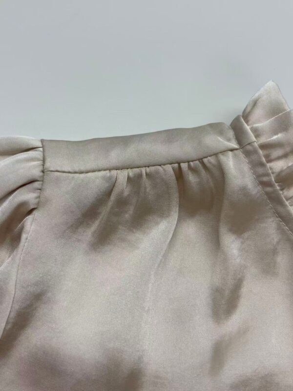 Close-up of a beige satin blouse with gathered shoulder detail, showcasing smooth fabric and subtle sheen, perfect for stylish fashion looks.