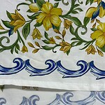 Close-up of fabric with vibrant yellow floral design and blue wave border, showcasing detailed hand-painted textile art.