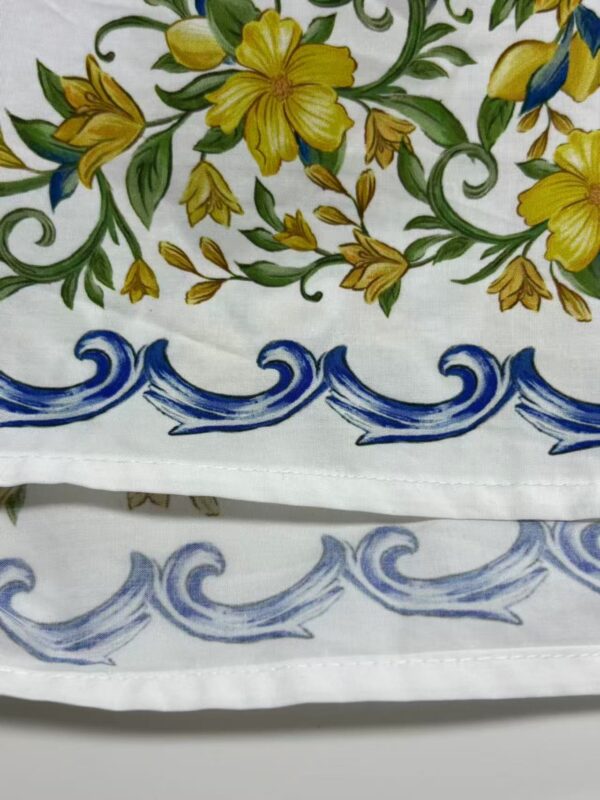 Close-up of fabric with vibrant yellow floral design and blue wave border, showcasing detailed hand-painted textile art.