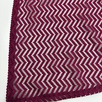 Close-up of magenta lace fabric with zigzag pattern, perfect for stylish clothing and accessories.