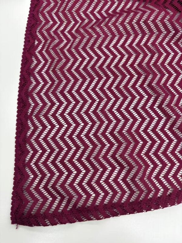 Close-up of magenta lace fabric with zigzag pattern, perfect for stylish clothing and accessories.