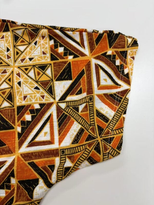Close-up of vibrant African tribal pattern fabric with geometric shapes in orange, black, and white, ideal for fashion and cultural clothing designs.