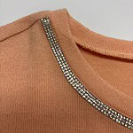 Close-up of peach-colored sweater featuring a rhinestone-embellished neckline for a stylish and elegant look.