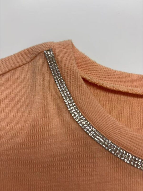 Close-up of peach-colored sweater featuring a rhinestone-embellished neckline for a stylish and elegant look.