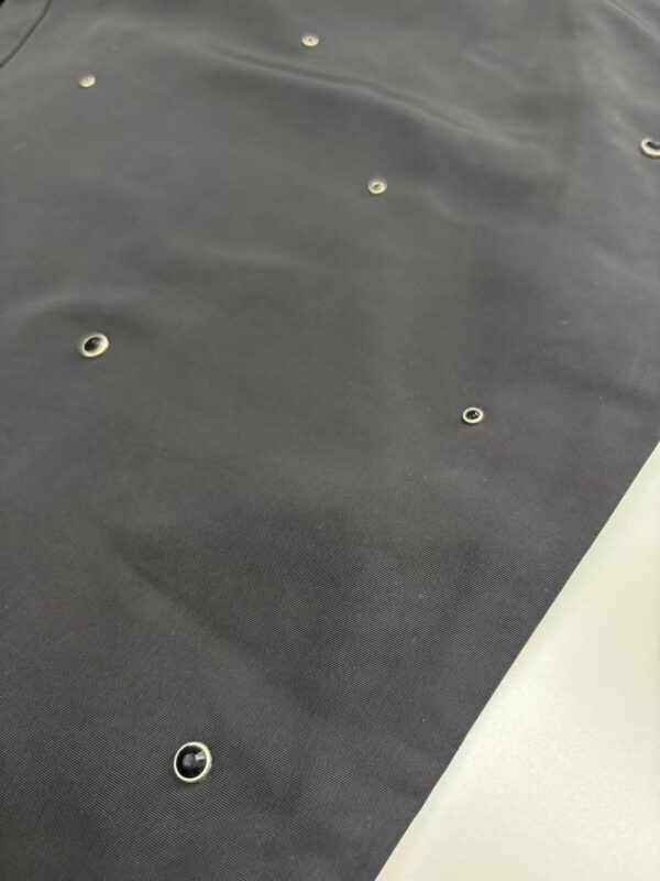 Close-up of black fabric with metal eyelets, suitable for fashion or accessory projects, showing texture and details.