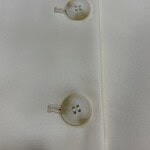 Close-up of two white buttons sewn onto a white fabric, showcasing fine stitching and smooth texture, ideal for fashion or clothing product images.