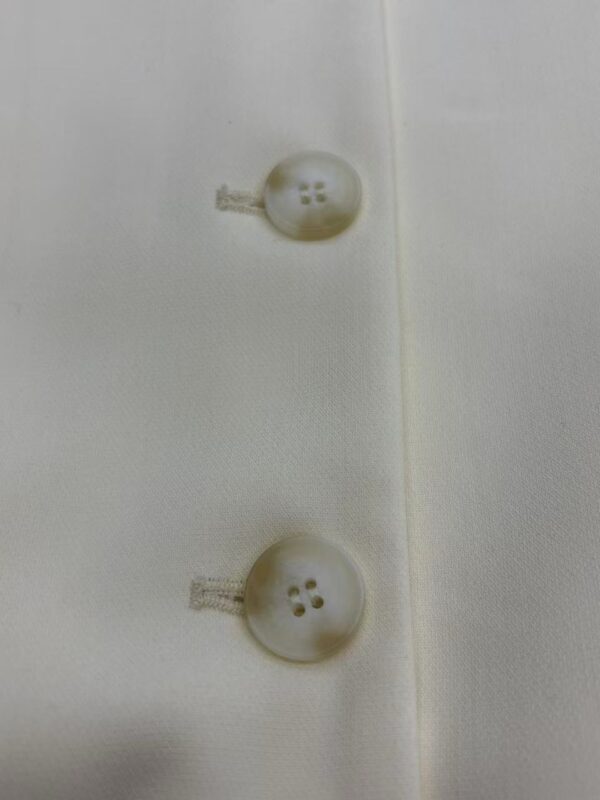Close-up of two white buttons sewn onto a white fabric, showcasing fine stitching and smooth texture, ideal for fashion or clothing product images.