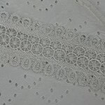 Close-up of white fabric with intricate embroidery and eyelet details, ideal for fashion and dressmaking projects.