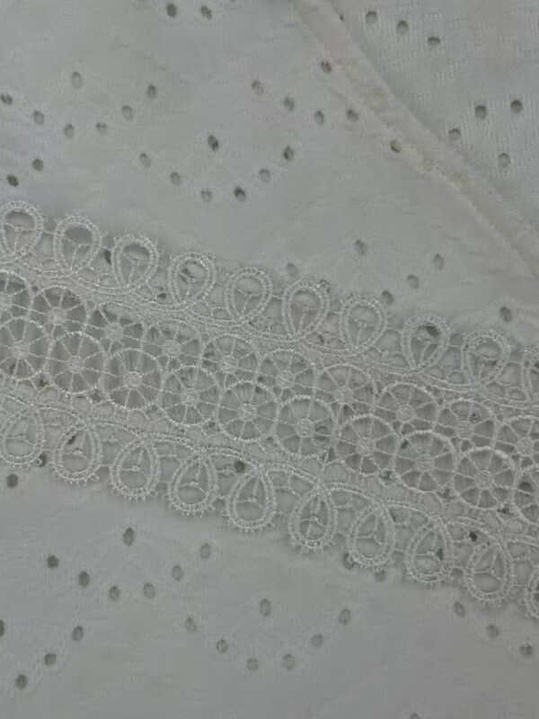 Close-up of white fabric with intricate embroidery and eyelet details, ideal for fashion and dressmaking projects.