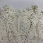 Close-up of an elegant ivory lace blouse with intricate patterns and pearl buttons, perfect for formal or special occasions.