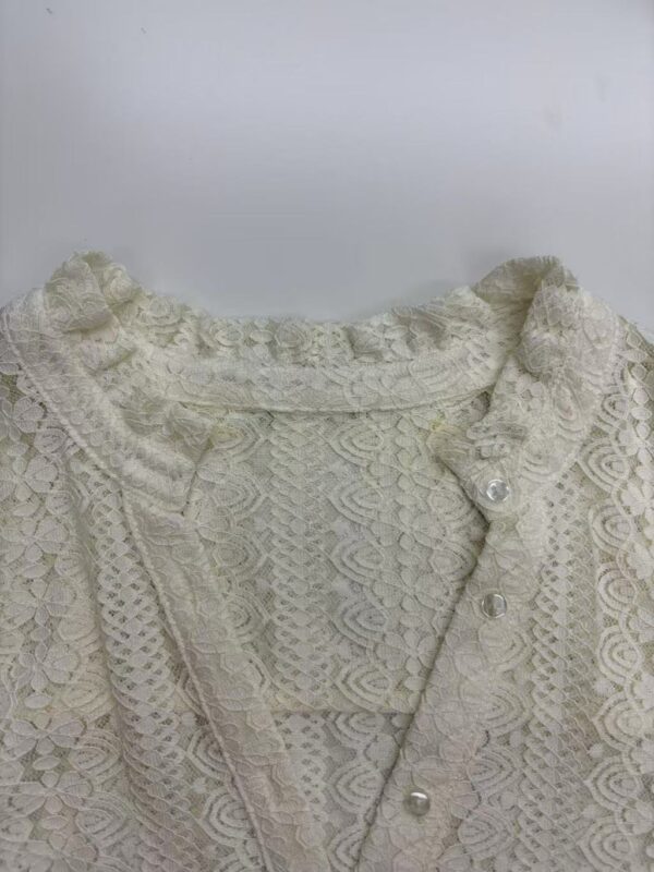 Close-up of an elegant ivory lace blouse with intricate patterns and pearl buttons, perfect for formal or special occasions.