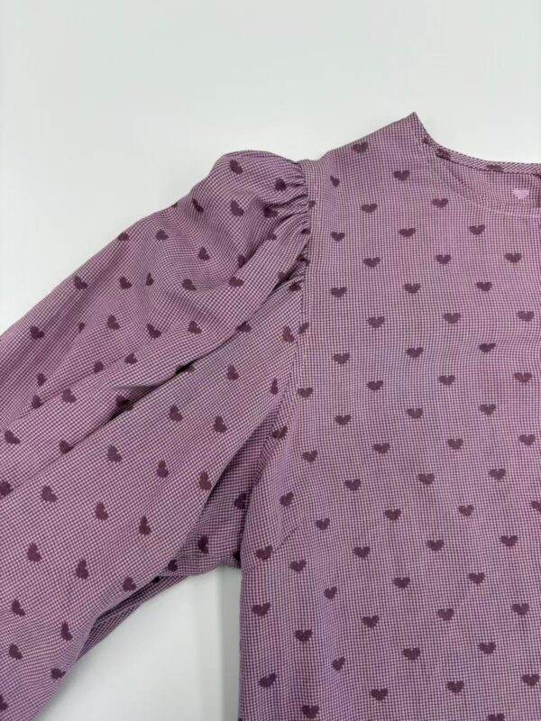 Close-up of a pink blouse with purple heart patterns and puffed sleeves, perfect for casual or semi-formal wear.