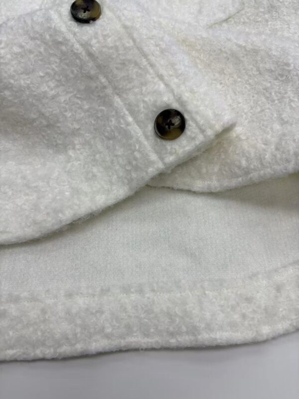 Close-up of a white wool coat featuring black buttons, showcasing high-quality fabric and craftsmanship, perfect for stylish winter wear.