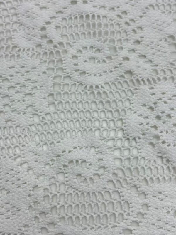 Close-up of intricate white lace fabric with floral and swirl patterns, ideal for fashion and dressmaking.
