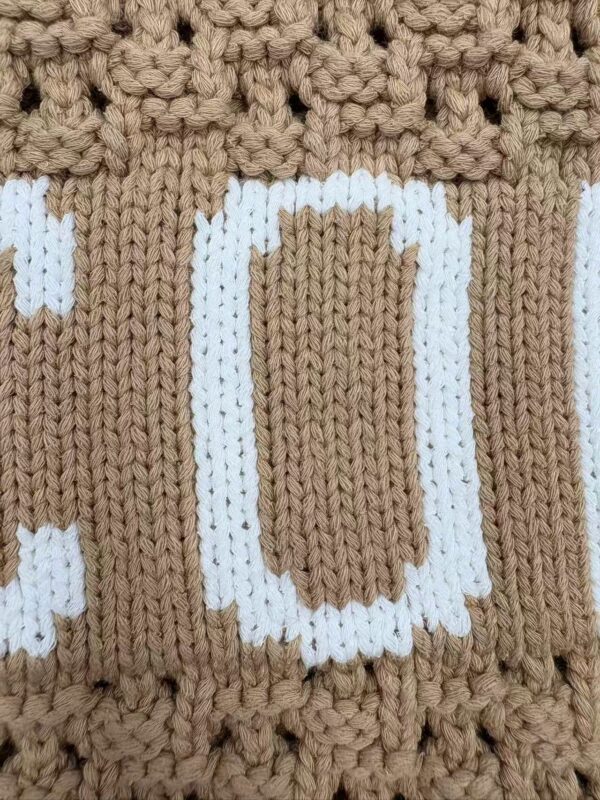 Close-up of a knitted fabric with a beer mug design in white on a brown background.