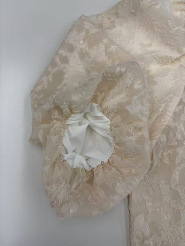 Close-up of luxurious lace fabric with intricate floral patterns and a ruffled satin detail, ideal for high-end fashion and bridal wear.
