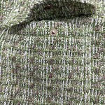 Close-up of a green and pink tweed jacket with a metallic button, showcasing textured fabric and stylish design for fashion enthusiasts.