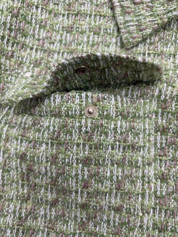 Close-up of a green and pink tweed jacket with a metallic button, showcasing textured fabric and stylish design for fashion enthusiasts.