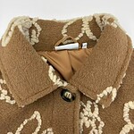 Close-up of a brown wool coat with white embroidered floral patterns, featuring a collar and a button closure, perfect for fall and winter fashion.