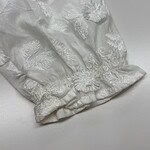 Close-up of white fabric with intricate floral embroidery and textured details, suitable for luxury fashion or bridal wear.